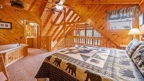 Una cabaña acogedora con interior de madera, una cama con colcha de temática de oso, un baño y un balcón con vistas.