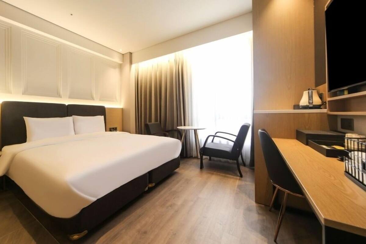A hotel room with a large bed, a desk, a chair, and a TV.