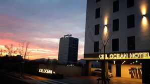 The exterior of the Cielocean Hotel with a clear view of the building's facade, a parking area, and a distant mountain. - Busan Myeongji Ciel Ocean Hotel (Busan)