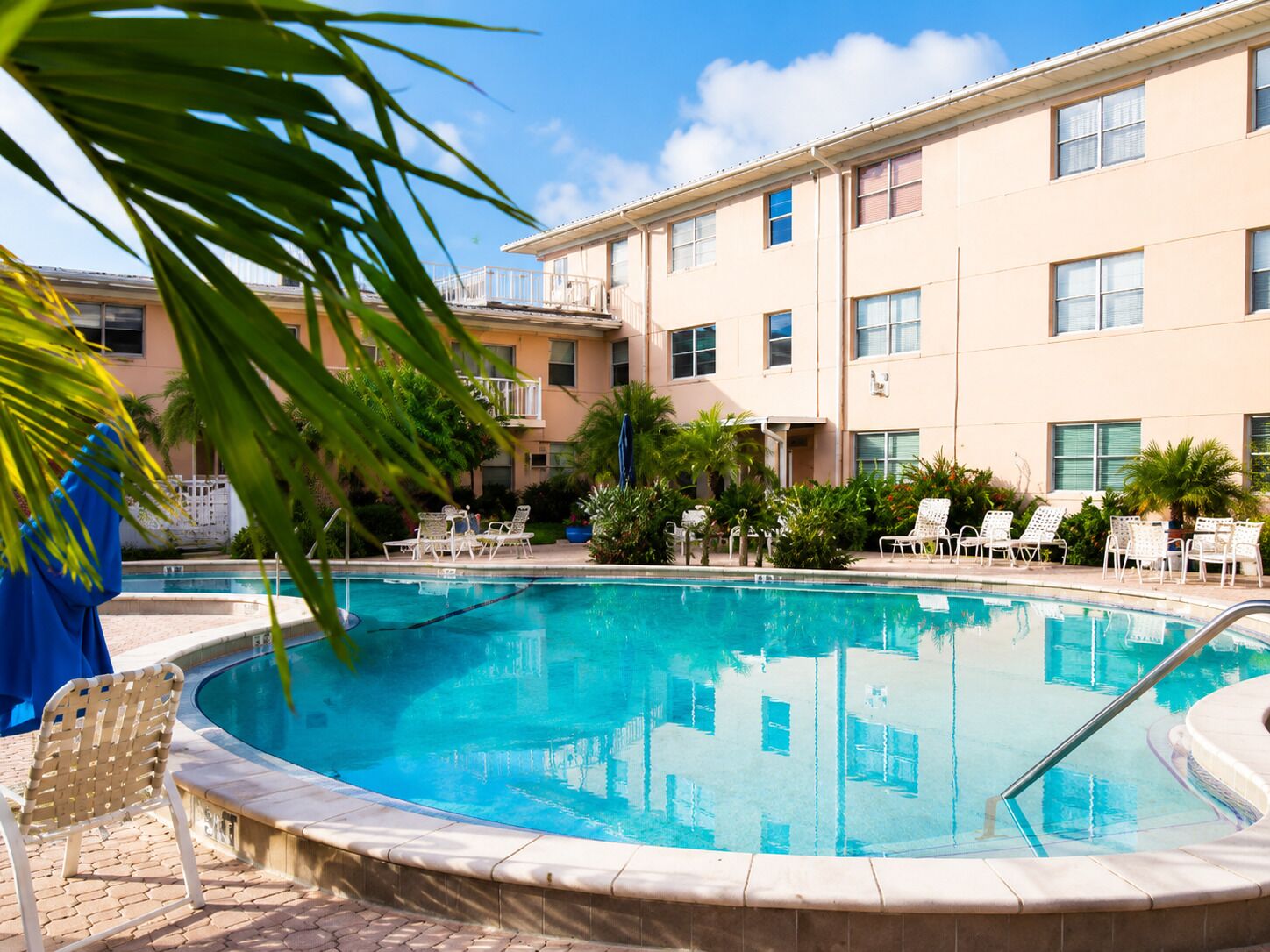A swimming pool with lounge chairs, a building with multiple windows, and a clear sky.