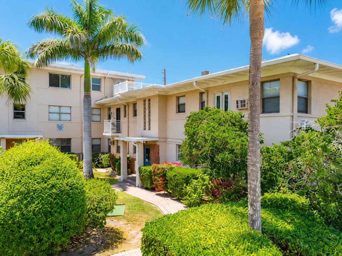 A multi-story building with balconies, surrounded by lush greenery and palm trees.