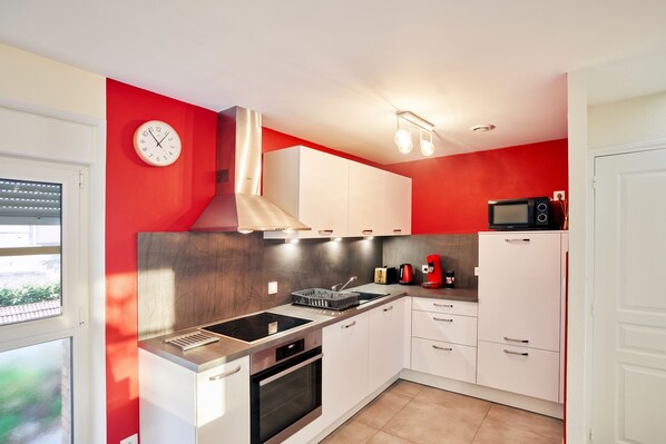 A compact kitchen with white cabinets, a stainless steel range hood, a built-in oven, a microwave, and a sink with a modern faucet.