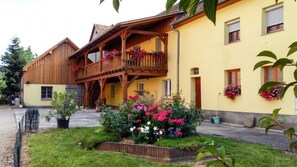 Ein Holzhaus mit einem Balkon, ein Garten voller Blumen und ein klarer Himmel.