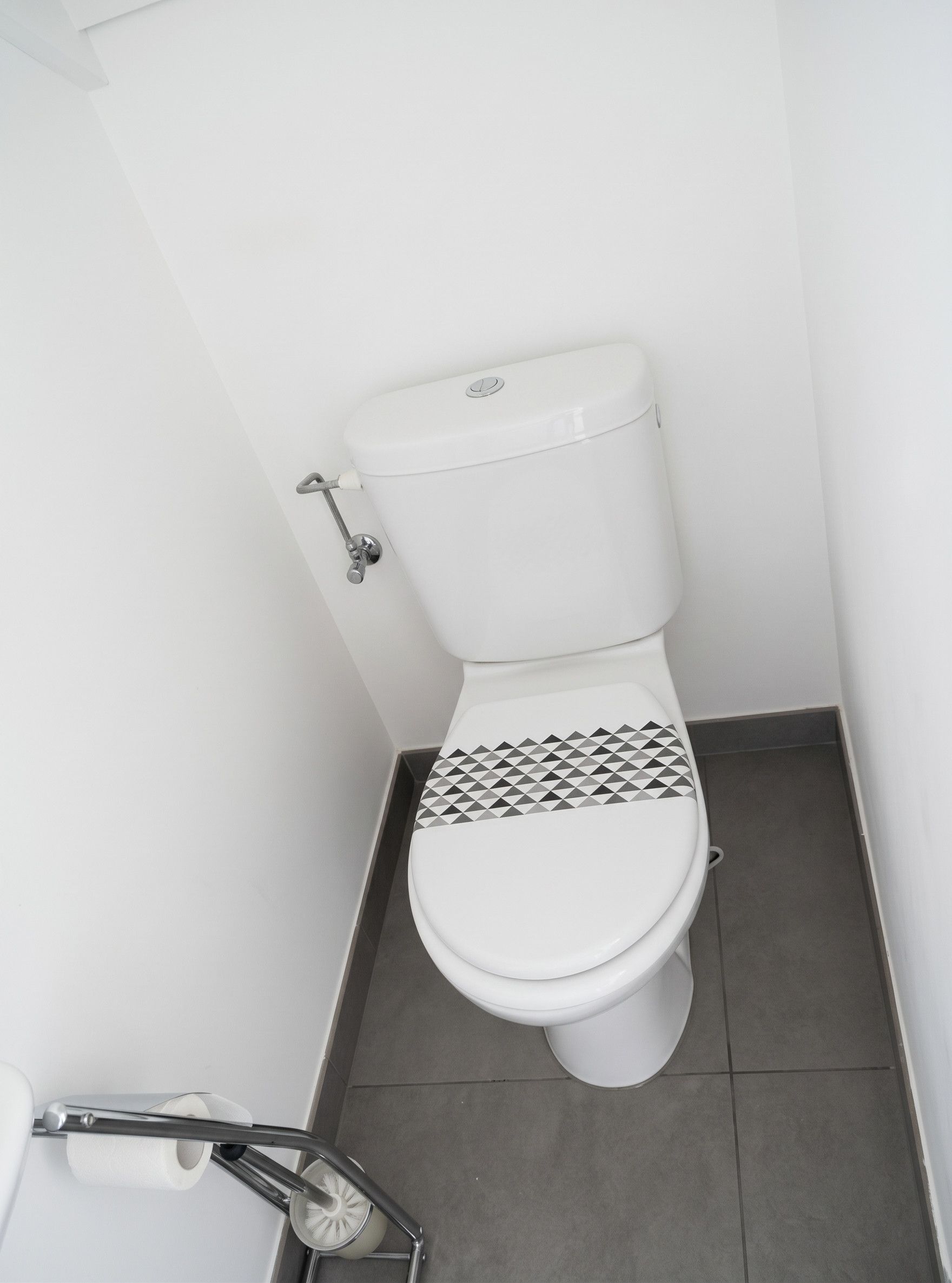 Eine weiße Toilette mit einem gemusterten Toilettensitz, einem Metall-Bidetaufsatz und einer Toilettenpapierrolle auf dem Boden.