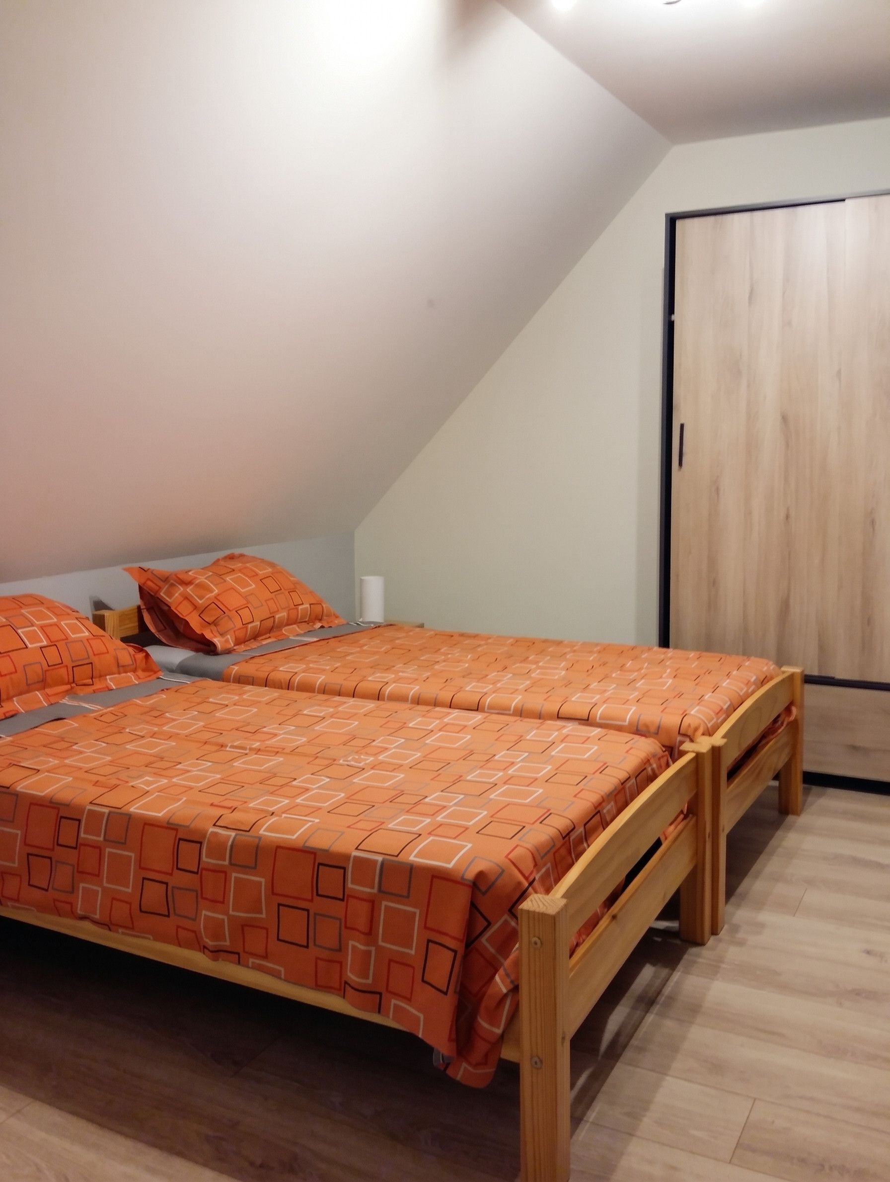 A bedroom with a sloped ceiling, a wooden bed frame, and a wooden wardrobe.