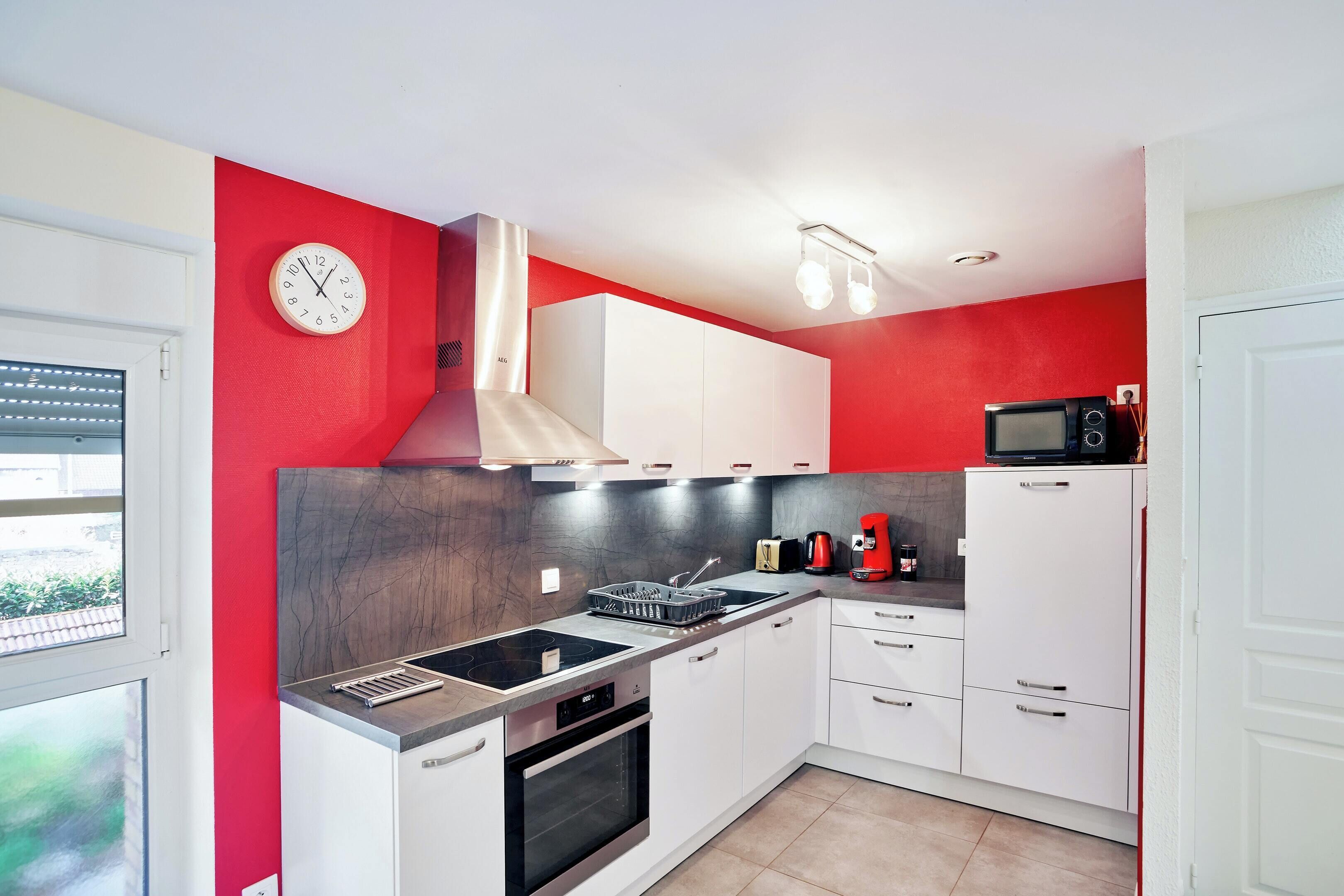 Una cucina moderna con mobili bianchi, una parete a contrasto rossa, un forno a incasso e un microonde.