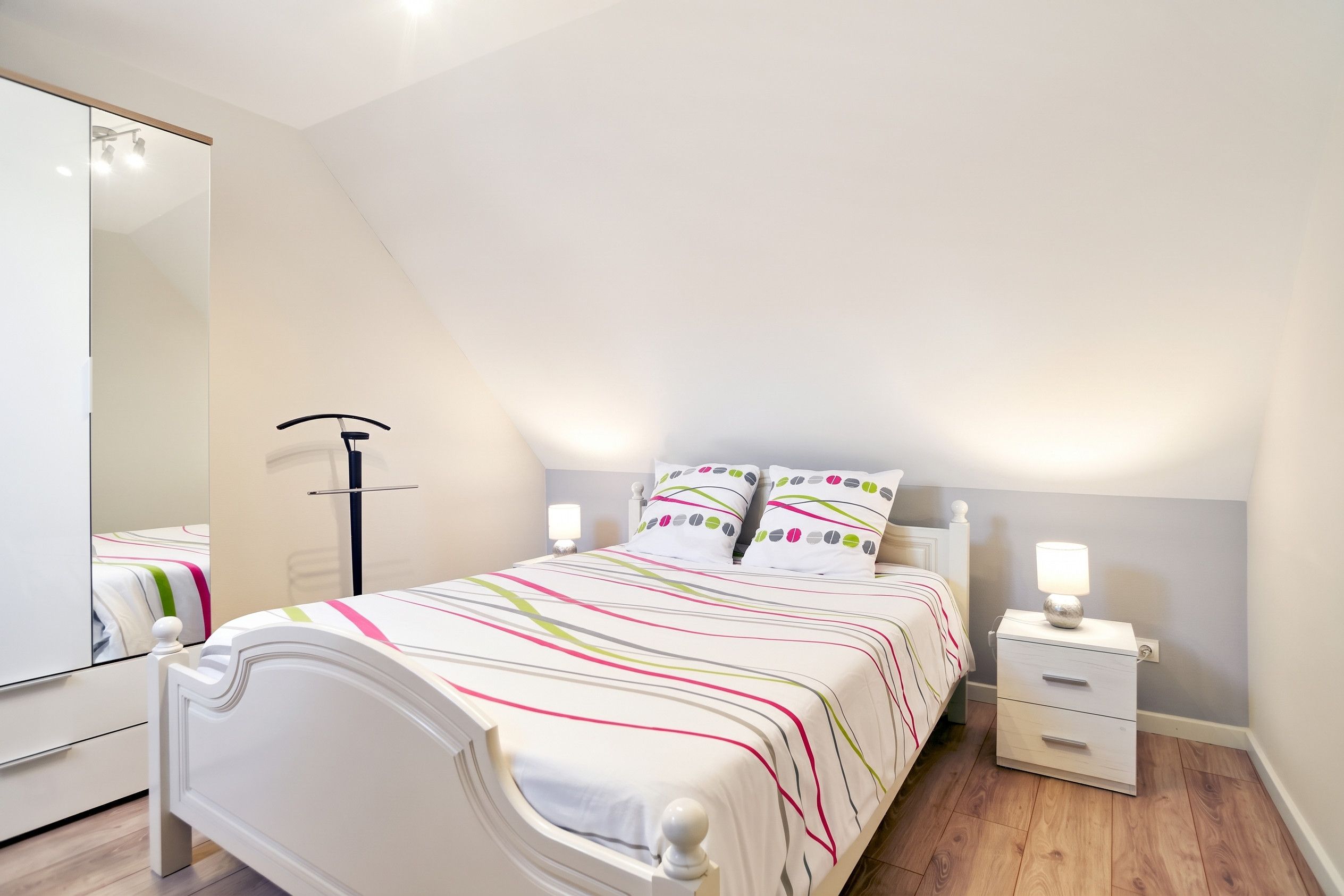 A bedroom with a bed, bedside tables, a mirror, and a lamp.