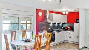 Cocina moderna con armarios blancos, una pared de acento roja y un comedor con sillas y mesa de madera.