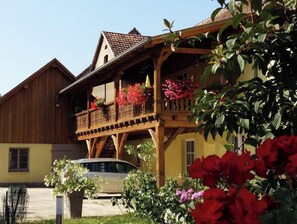 Ein traditionelles Chalet mit Holzbalkon, einem geparkten Auto davor und einem blumenbewachsenen Garten.