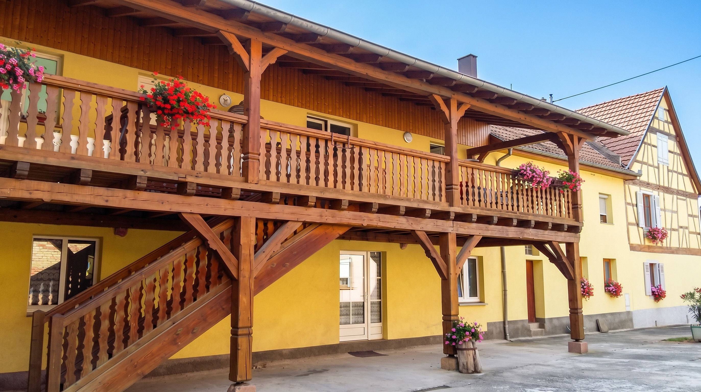 A traditional wooden balcony with a staircase, yellow walls, and flower boxes.