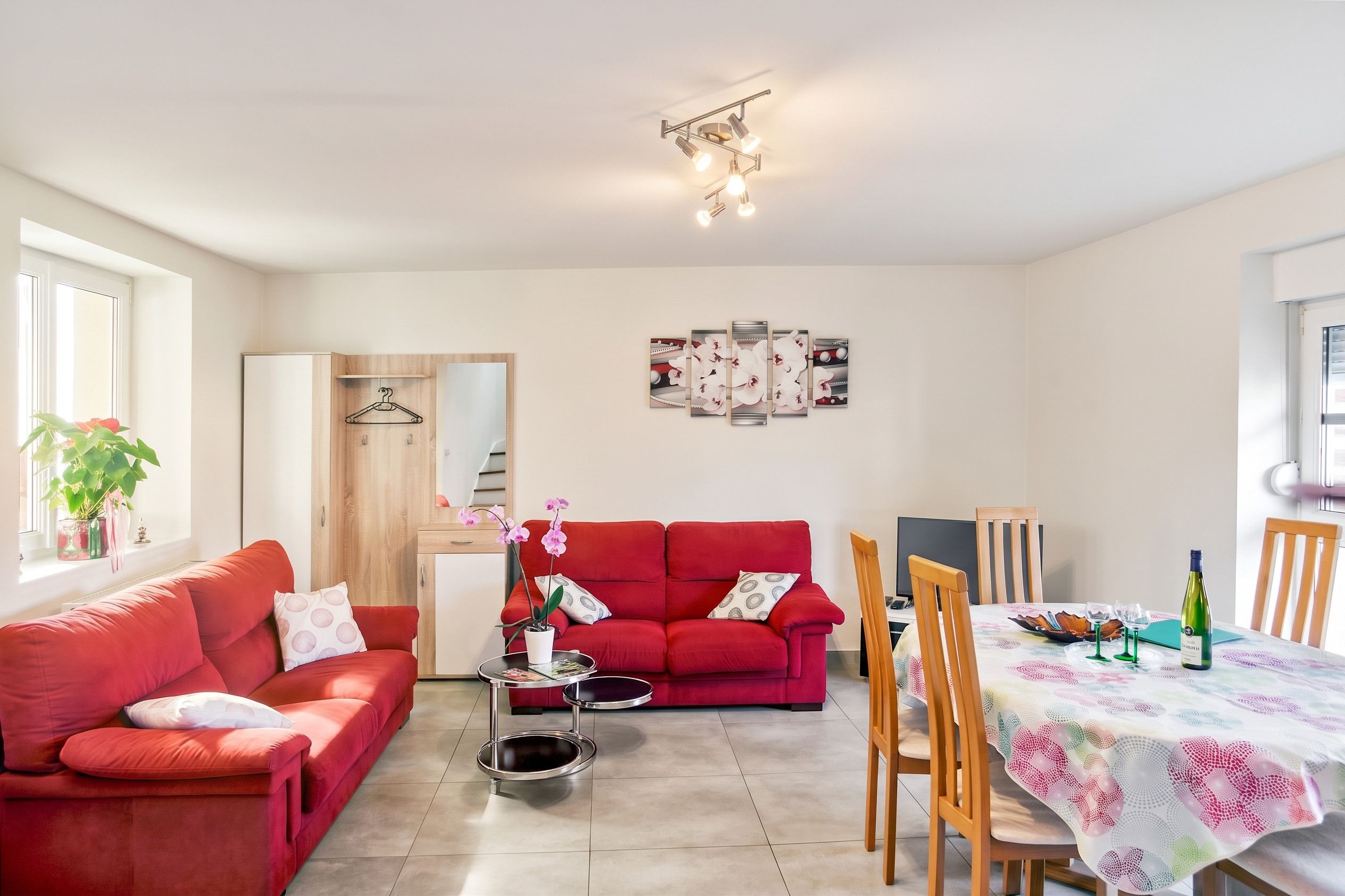 A modern living room with a red sofa, a dining table with chairs, and a ceiling light fixture.