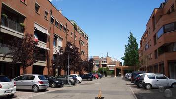 Un parking où sont garées plusieurs voitures devant une rangée d’immeubles en briques dotés de balcons.