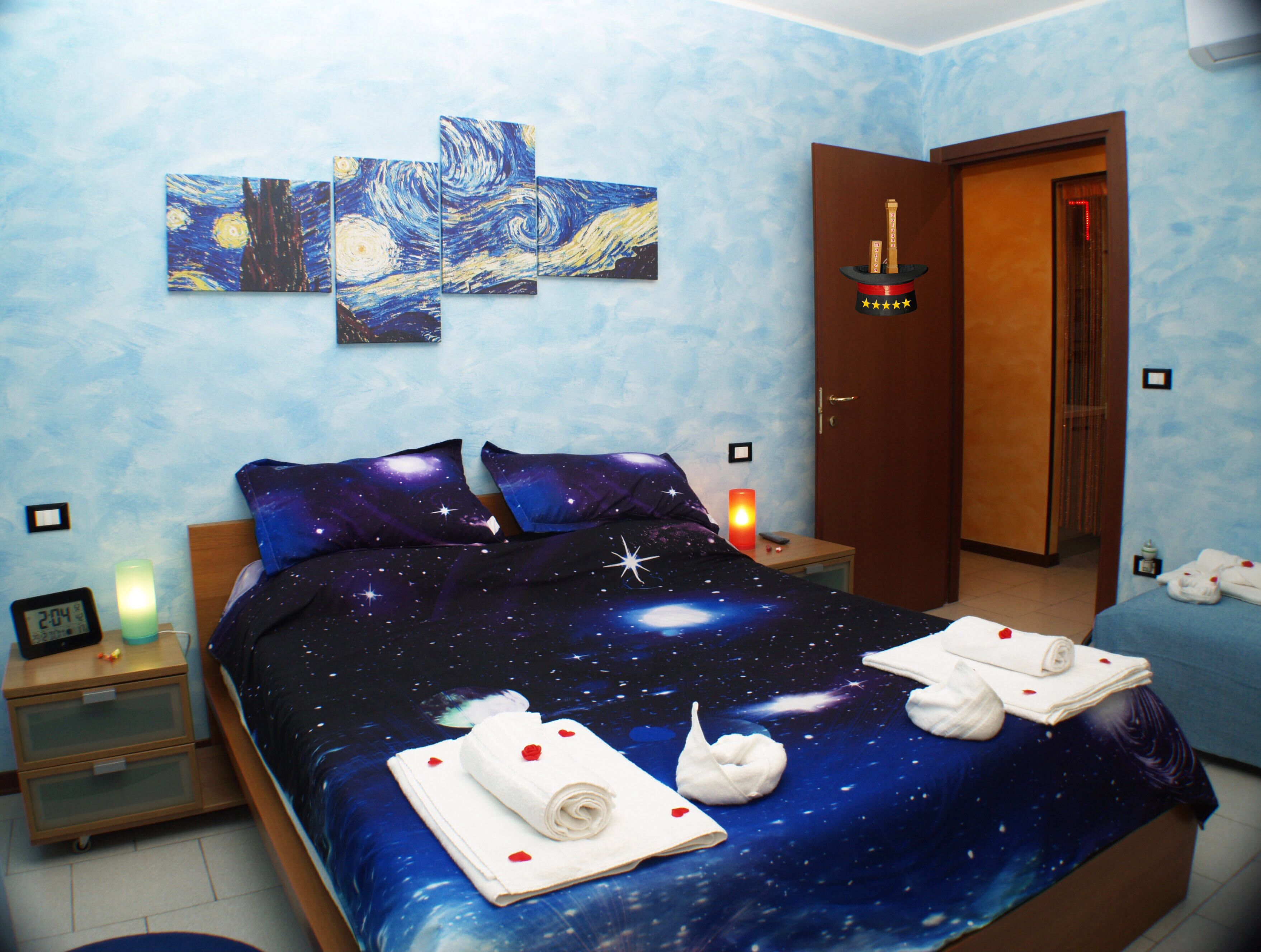Ein Schlafzimmer mit einem zudeckenden Bett mit Sternenmuster, einem Bild an der Wand und einem Nachttisch mit Lampe.