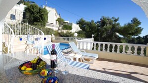 A terrace with a pool, lounge chairs, and a table with fruit bowls and a bottle of wine. - Vacation home Alexia by Interhome (Benissa)