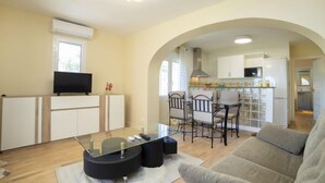 A modern living room with a glass coffee table, a sofa, and a TV on a cabinet. There is a kitchen area with white cabinets and a dining table with chairs. - Vacation home Alexia by Interhome (Benissa)