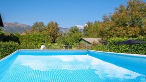 Une piscine rectangulaire à l’eau d’un bleu cristallin, entourée de verdure et offrant, en arrière-plan, une vue sur les montagnes.