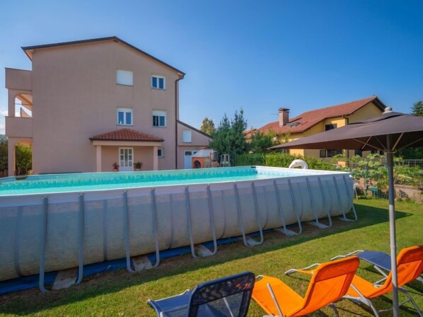 A swimming pool with a covered area, surrounded by grass and outdoor furniture. - Apartment Rita by Interhome (Rijeka)