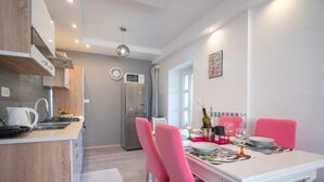 Une cuisine moderne avec des meubles blancs, un réfrigérateur en acier inoxydable et un coin repas comprenant une table blanche et des chaises roses.