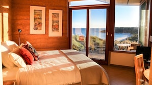 Une chambre avec un grand lit, deux œuvres d’art encadrées, une table de chevet et une vue sur la mer, visible à travers une porte-fenêtre coulissante.