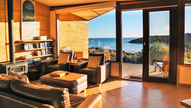 Un salon moderne doté d’une grande porte-fenêtre coulissante qui donne sur une terrasse offrant une vue sur la mer.