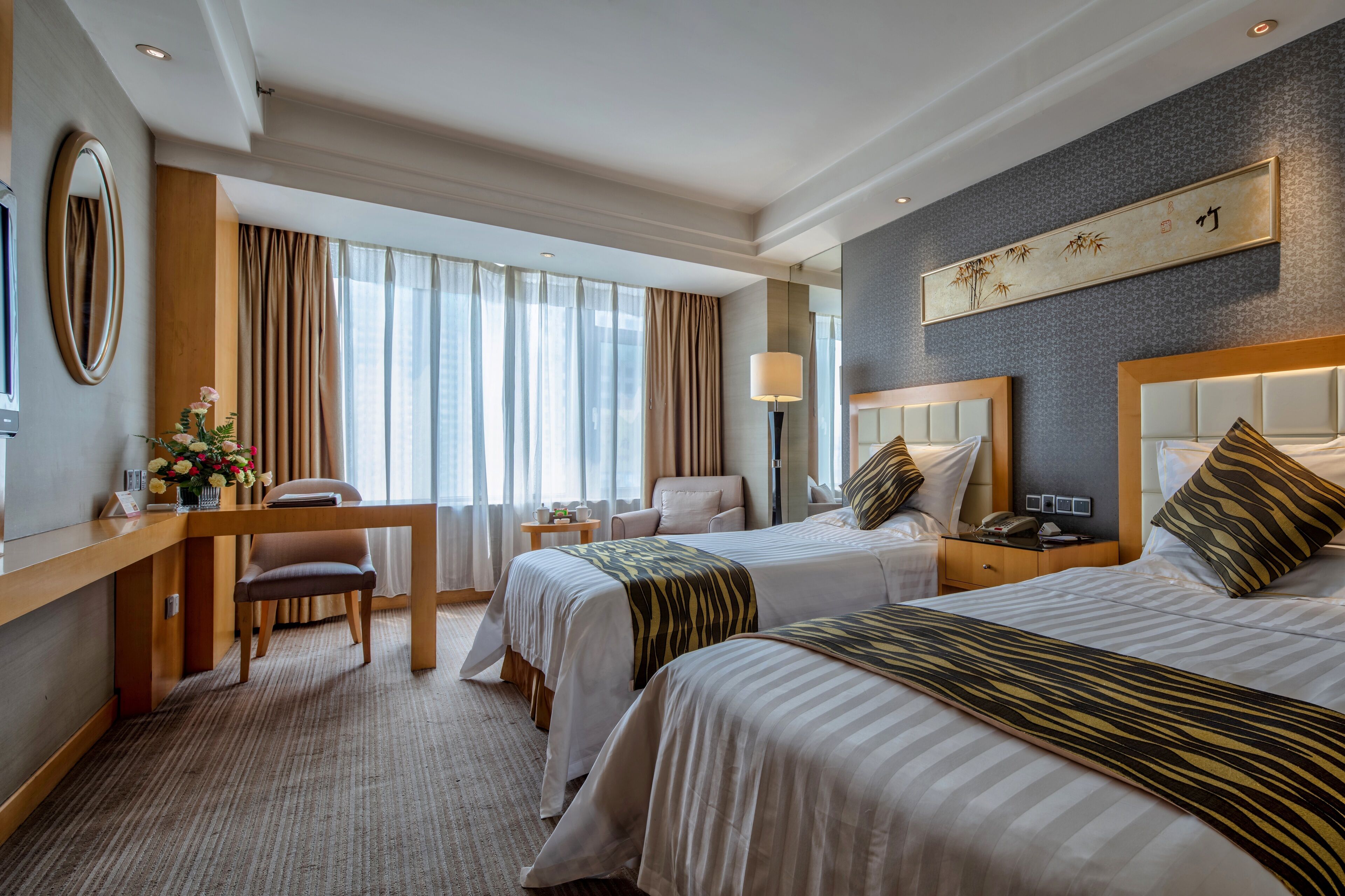 Habitación de hotel con dos camas, un escritorio, una silla, una lámpara y una obra de arte grande en la pared.
