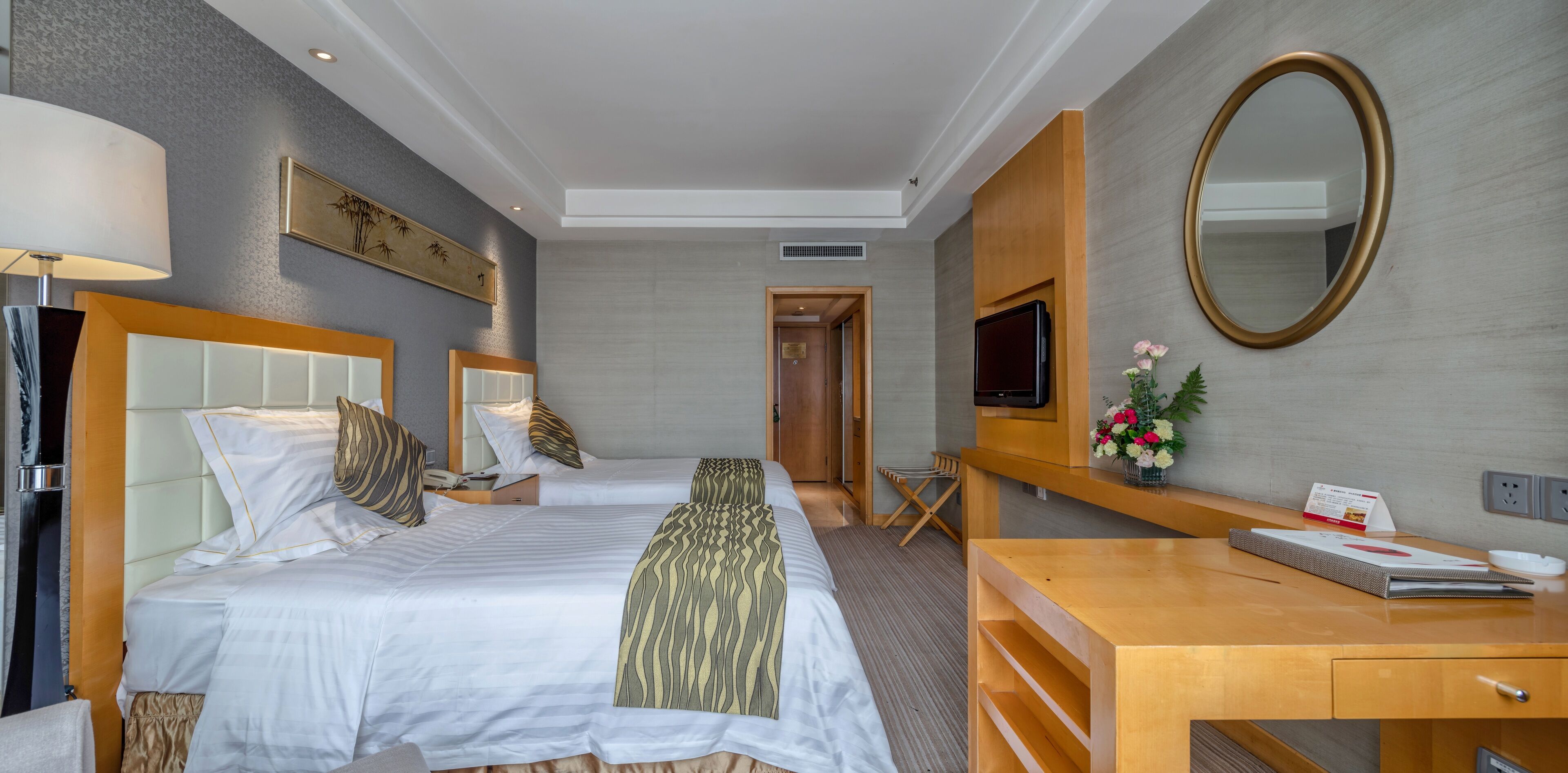Una habitación de hotel con dos camas, un escritorio de madera, un televisor y un espejo.