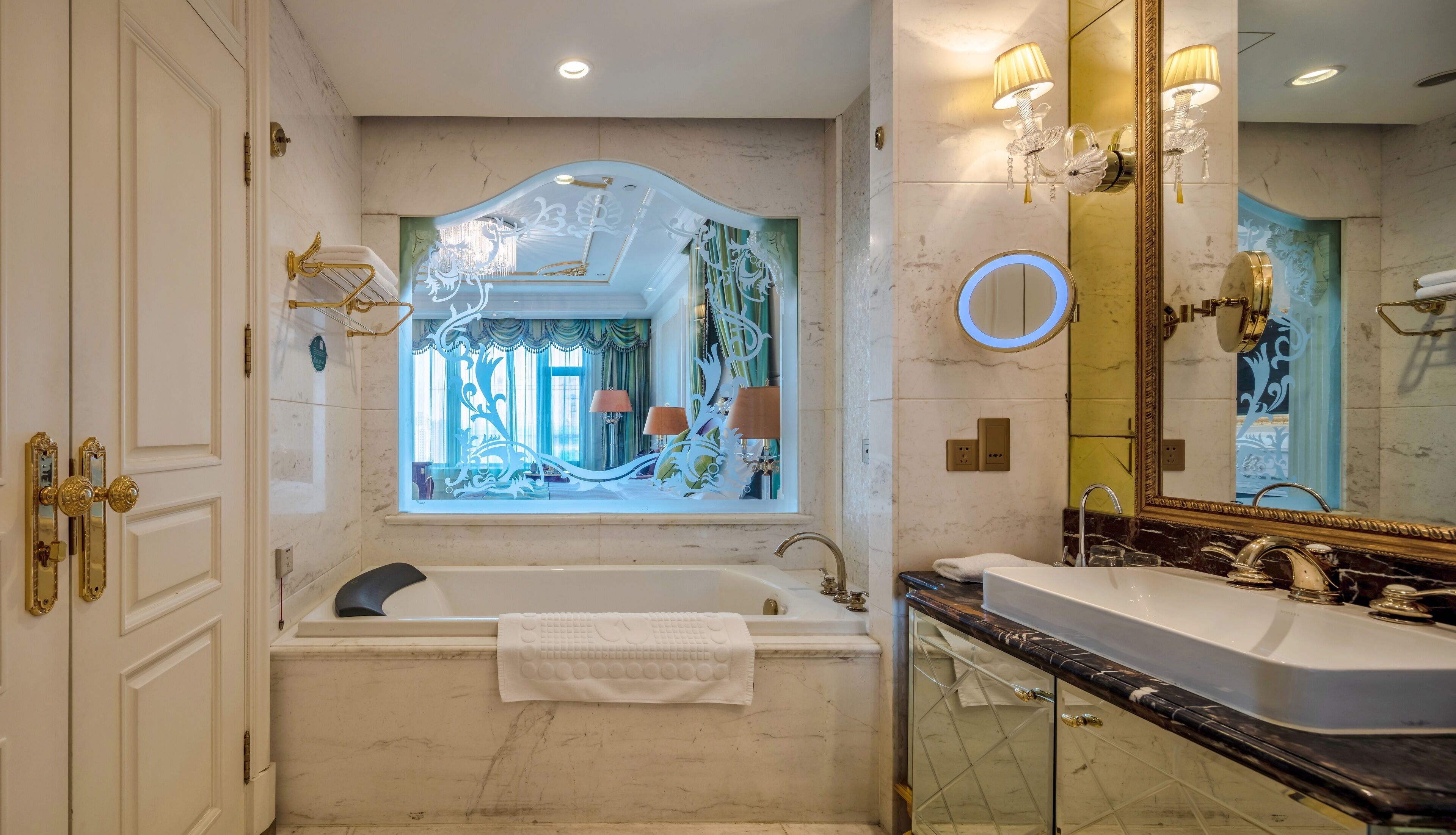 Un baño lujoso con una bañera grande, un lavamanos aparte y un espejo con marco dorado.