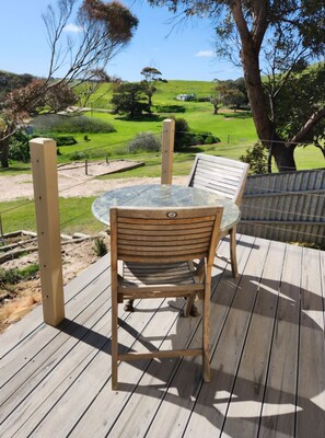 A wooden deck with a table and chairs, overlooking a green landscape with hills and trees. - Settlers Cottage - Snellings Beach - Kangaroo Island (Middle River)