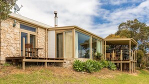 A stone house with large windows, a chimney, and a deck with outdoor furniture. - Settlers Cottage - Snellings Beach - Kangaroo Island (Middle River)