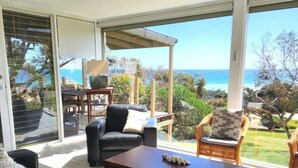 A modern living room with a large glass door leading to a balcony with a view of the sea. - Settlers Cottage - Snellings Beach - Kangaroo Island (Middle River)