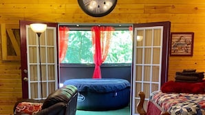 A cozy room with a wooden ceiling, a bed, a chair, a bean bag, and a large window with curtains. -  hot tub, grill, fireplace, Hocking Hills, Buckeye Lake, Legend Valley (Somerset)