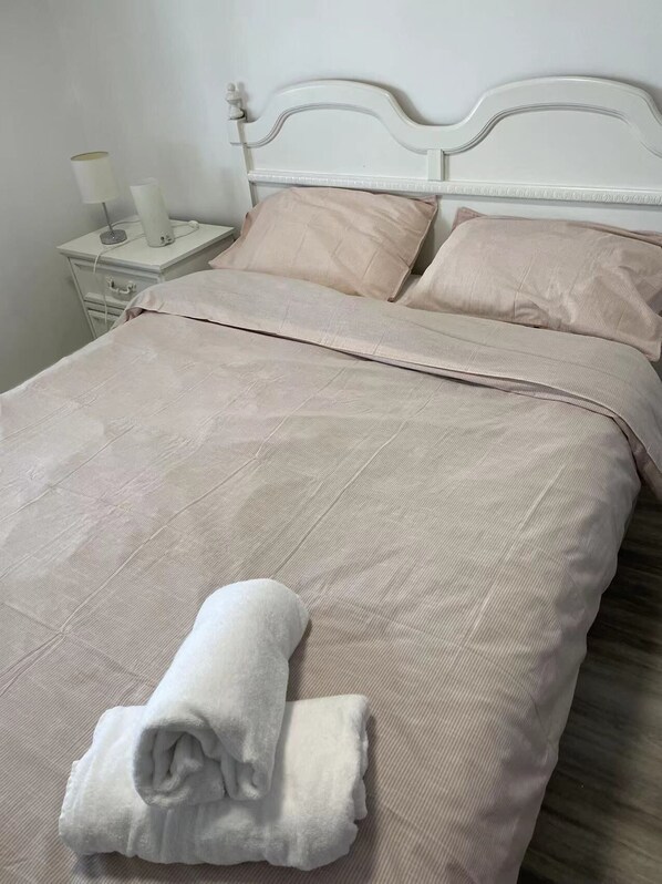 A neatly made bed with a beige bedspread and pillows, a white headboard, and a bedside table with a lamp and a small decorative item. - Lake Erie waterfront cottage (Blenheim)