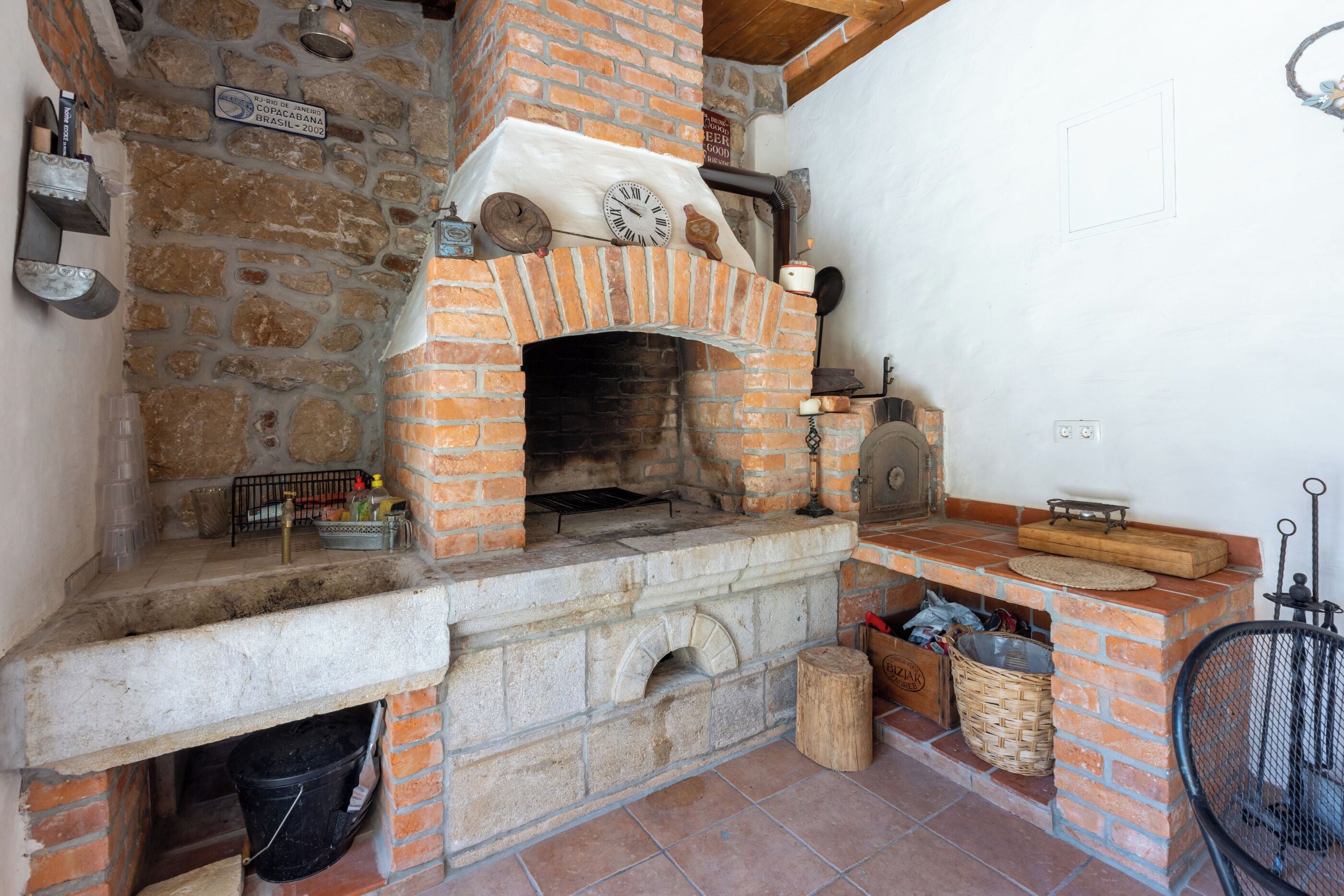 A stone and brick fireplace with a clock, a brick oven, and a stone sink.