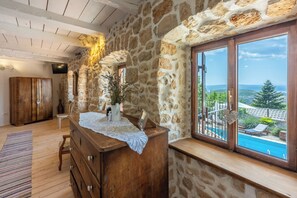Une pièce aux murs de pierre, avec une commode en bois, une petite table et une vue sur une piscine.