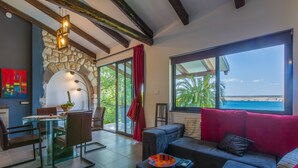 A modern living room with a glass dining table, comfortable seating, a large window with a view of the sea, and a stone wall. - Villa Fun Haus 2 (Jadranovo)