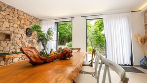 Un espace repas comprenant une table en bois, des chaises, un mur en pierre et de grandes fenêtres.