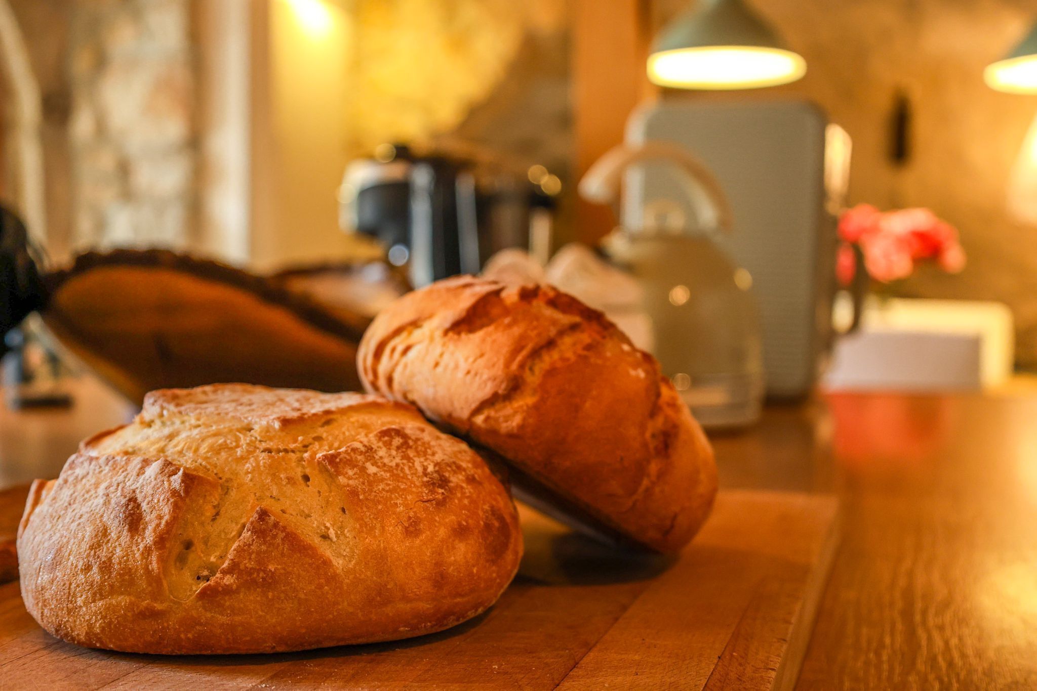Zwei Brotlaibe auf einem Holztisch, im Hintergrund ein Wasserkocher und eine Tasse.