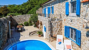 Un bâtiment en pierre doté d’une piscine, d’un espace extérieur aménagé et de volets bleus.