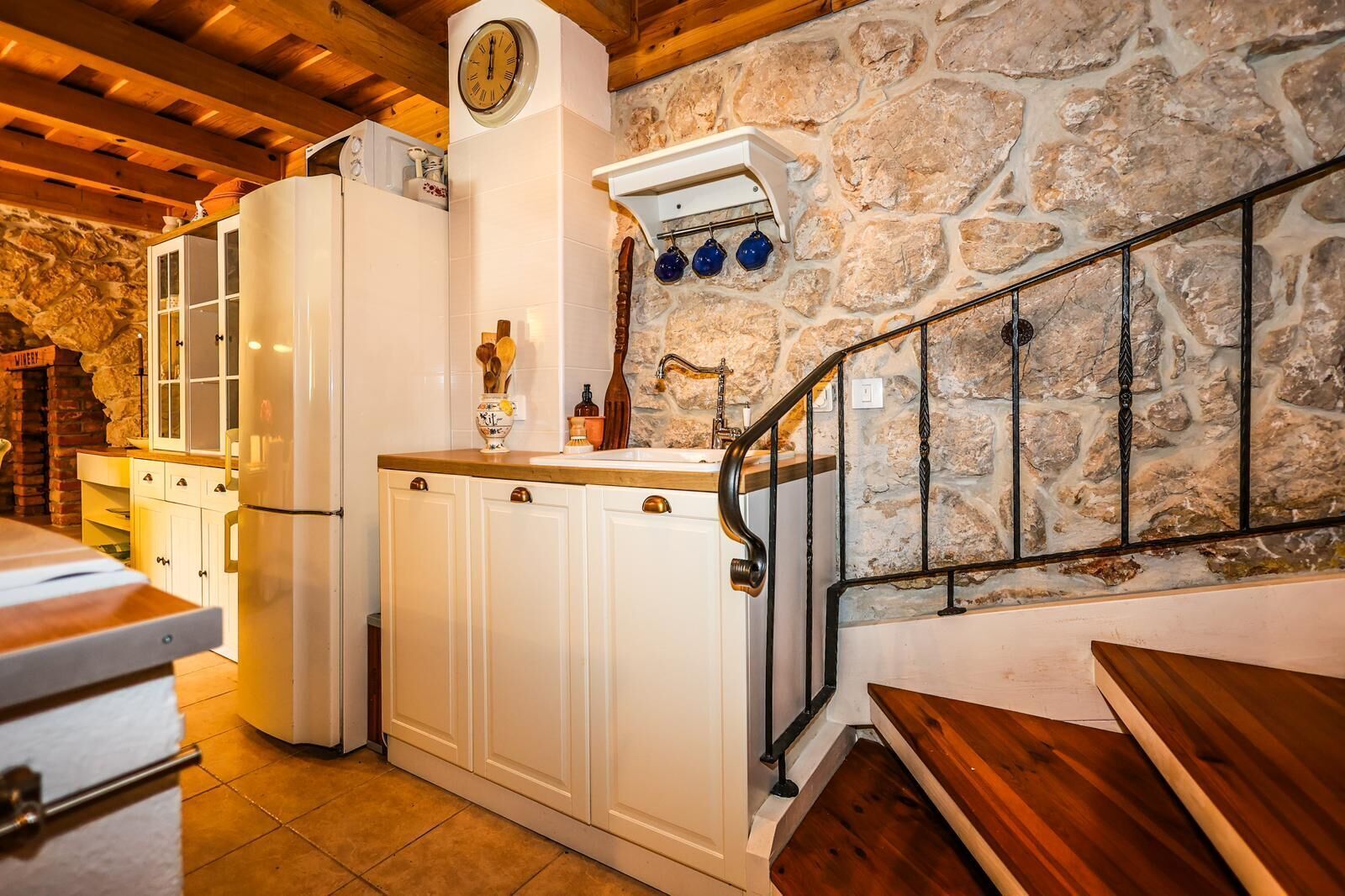 A rustic kitchen with stone walls, wooden beams, and white cabinetry.