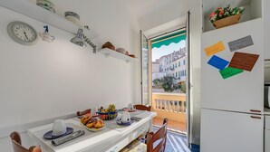 Una cuina petita amb taula de menjador, cadires, nevera i finestra amb vistes a edificis.