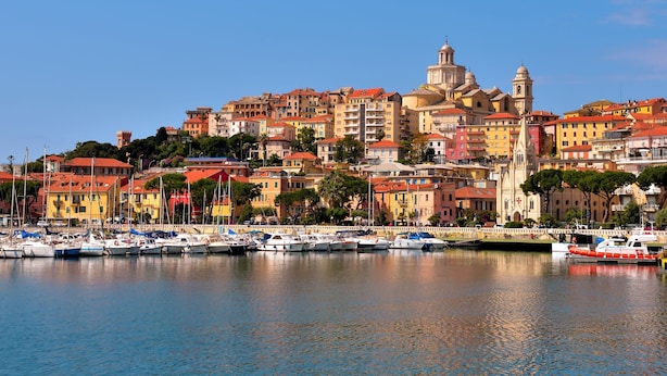 Un poble costaner amb edificis de colors, una església destacada i un port esportiu ple de vaixells.