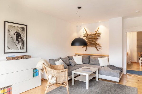 A modern living room with a sofa, a coffee table, a wicker chair, a white cabinet, and a wall-mounted lamp.