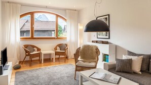 Een moderne woonkamer met een groot raam, rieten meubels, een witte bank en een zwarte hanglamp.
