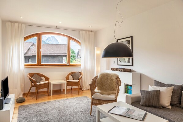 A modern living room with a large window, wicker furniture, a white sofa, and a black pendant light.