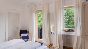 Een slaapkamer met twee bedden, een stoel met handdoeken, een raam met gordijnen en een radiator.