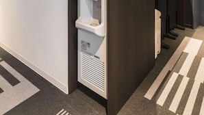 Moderni hotellikäytävä, jossa on juomavesiautomaatti ja roskakori.