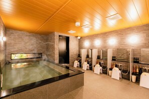 Un espace spa moderne doté d’un jacuzzi entouré de parois de verre, de plusieurs vasques et d’un plafond en bois.