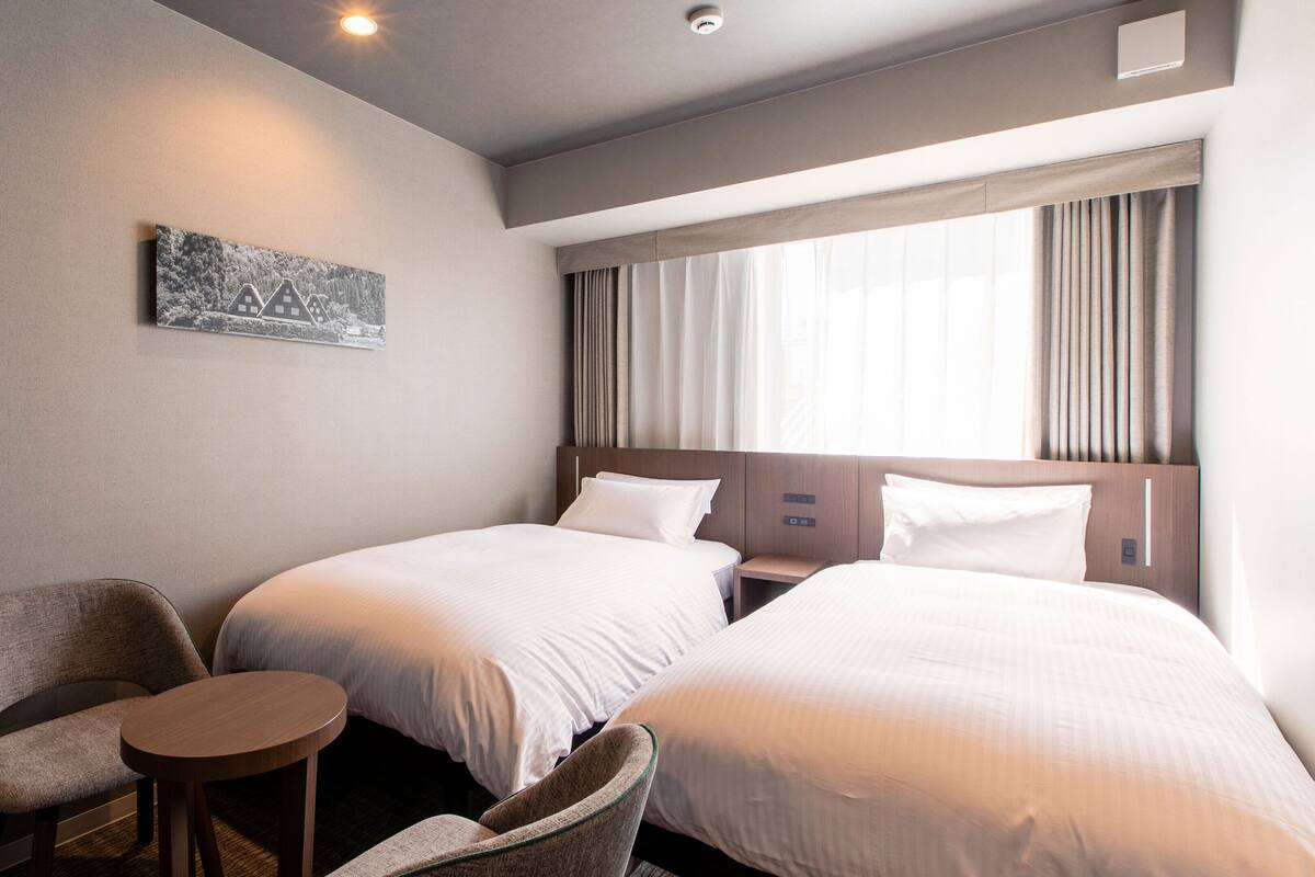 Een hotelkamer met twee bedden, een tafeltje en een stoel.