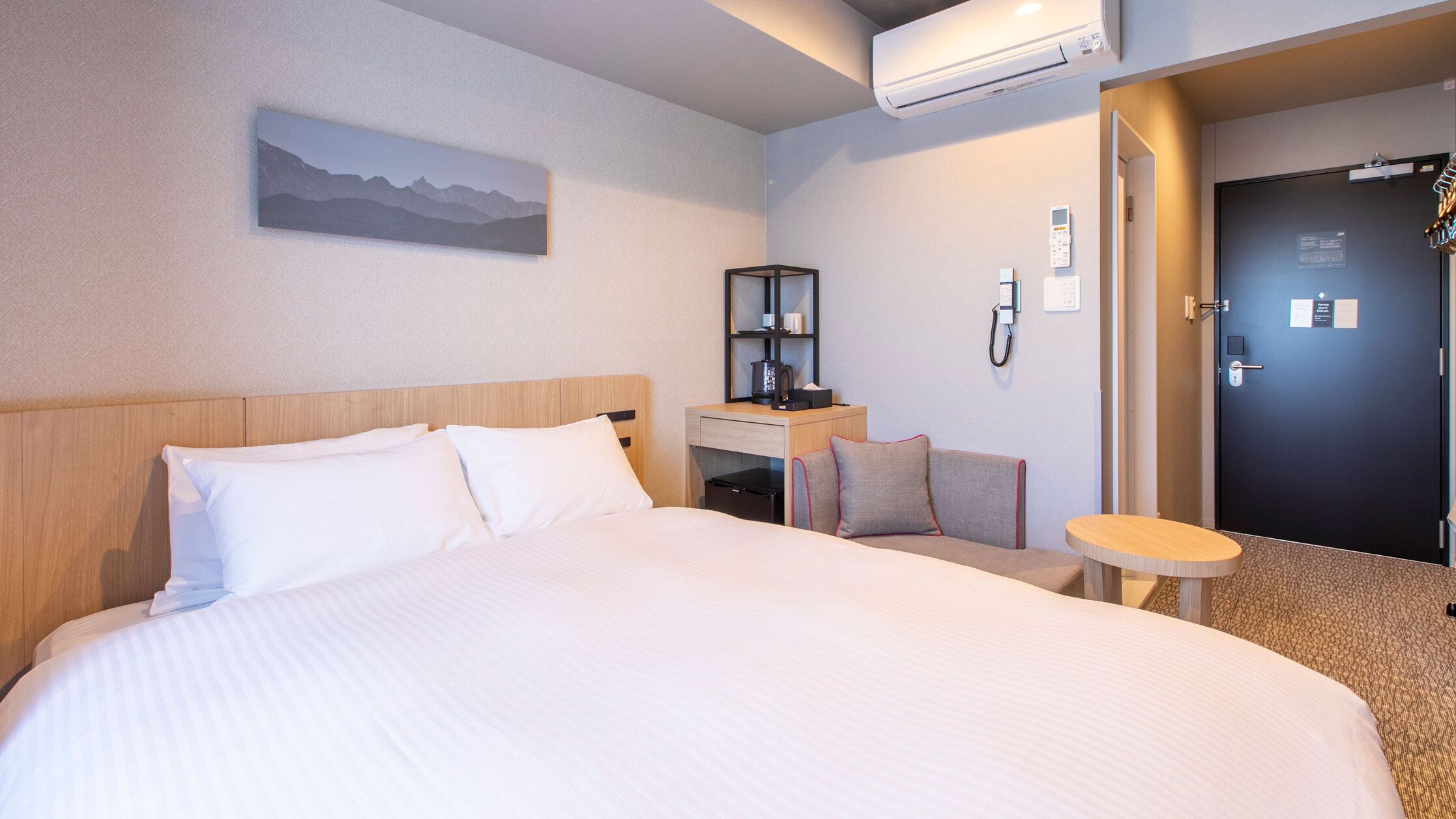 Ein Hotelzimmer mit einem großen Bett, einem Schreibtisch mit Stuhl, einem kleinen Tisch und einer Tür.