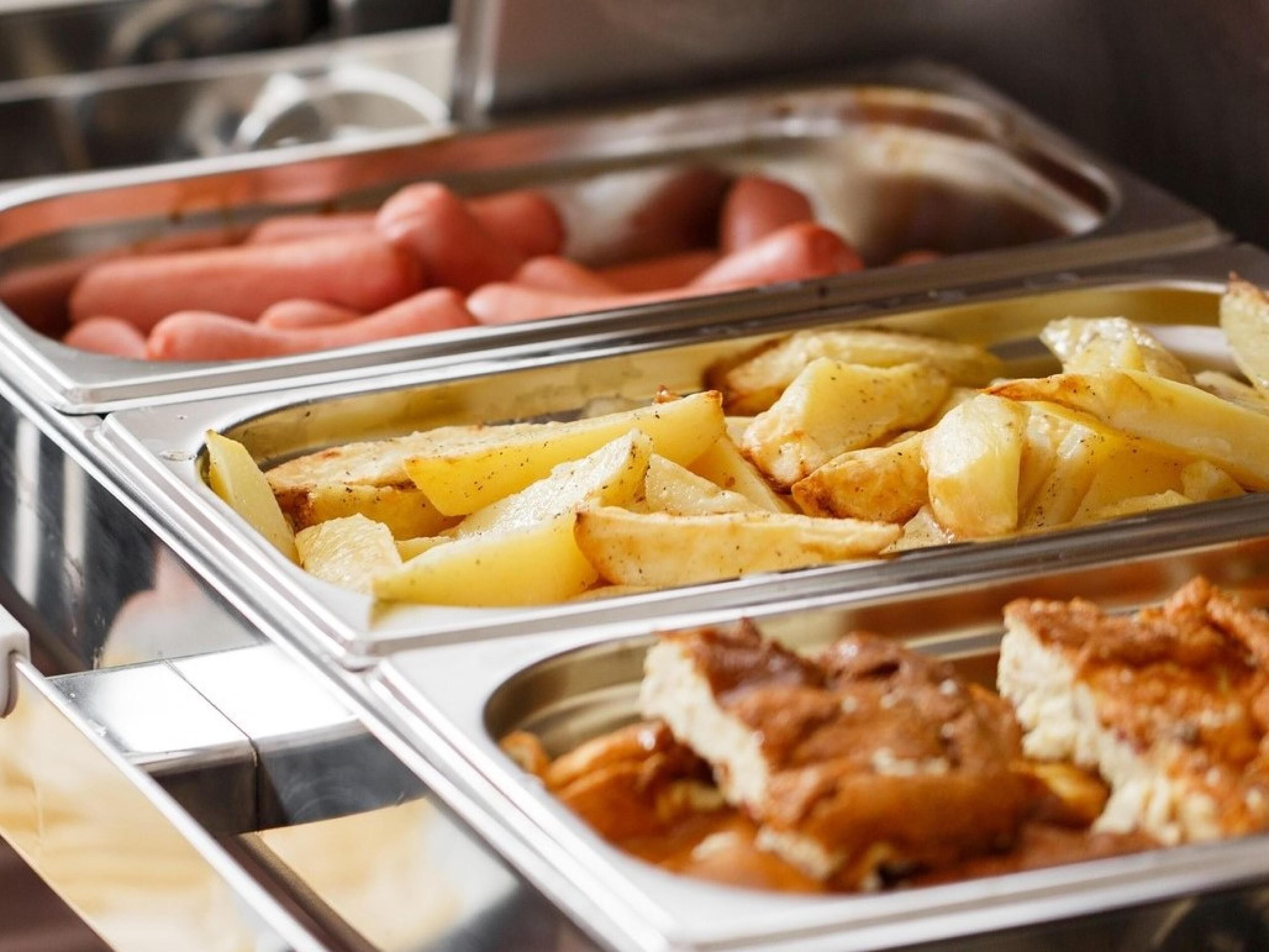 En buffé med ett varierat utbud av mat, inklusive potatis, korv och en kötträtt.